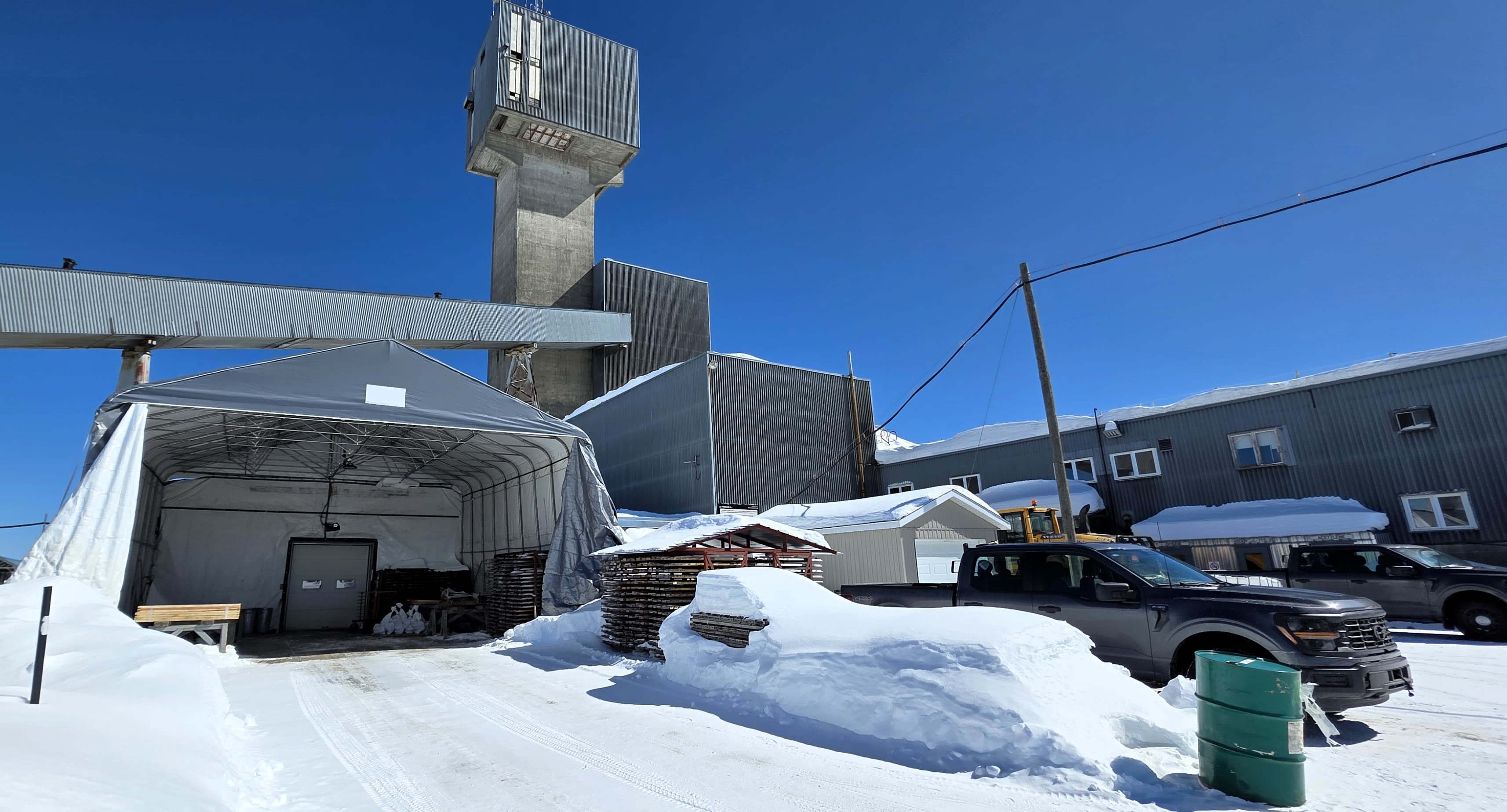 Espace d'entreposage, de description et d'échantillonnage des carottes de forage au diamant en premier plan, située dans les locaux de l'usine de Matagami Lake, avec le shaft de la mine historique et le convoyeur de la ligne de concasseurs de l'usine en arrière-plan